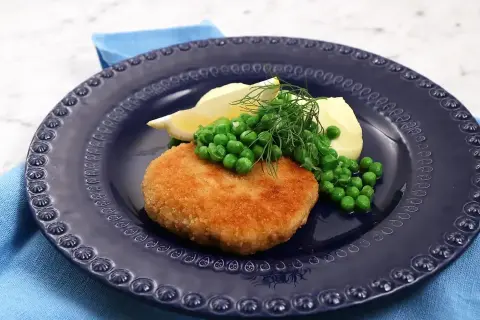 En gyllene havets wallenbergare serveras med potatis, gröna ärtor, citronklyfta och dill på en mörkblå tallrik.