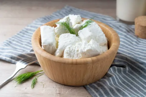 Półmisek z twarogiem półtłustym, udekorowany koperkiem. Obok widelec i szklanka mleka. Idealny na lekki posiłek, z niską zawartością kcal.