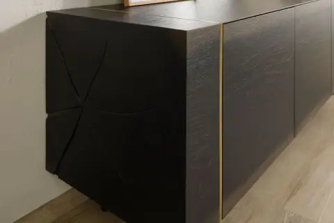Dunkles Sideboard mit markanter, geometrischer Front. Die Maserung des Holzes und die goldene Leiste unterstreichen, was bedeutet massiv: ein Möbelstück, das Charakter und Beständigkeit ausstrahlt.