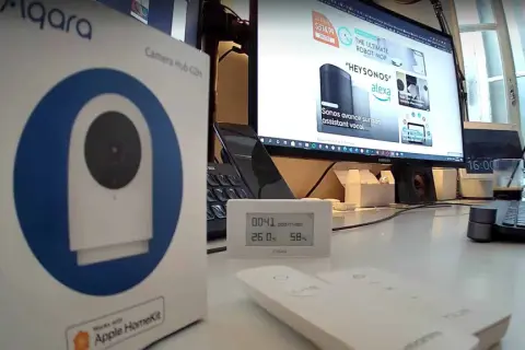 Boîte de l'aqara g2h pro, un hub caméra HomeKit, posée sur un bureau avec un écran d'ordinateur affichant des produits domotiques.