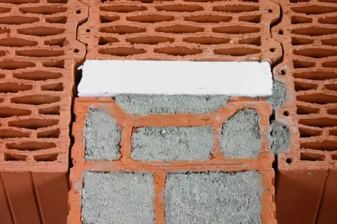 Zbliżenie na pustaki ceramiczne z zaprawą i białym elementem izolacyjnym.