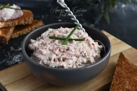 Un bol de rillettes de thon crémeuses, garnies de ciboulette, prêtes à être tartinées sur du pain grillé.