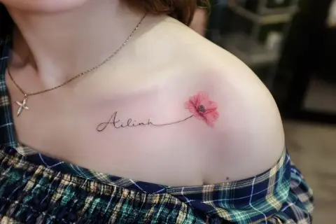 Ein zartes Tattoo mit dem Namen "Ailinh" und einer roten Mohnblume auf der Schulter.