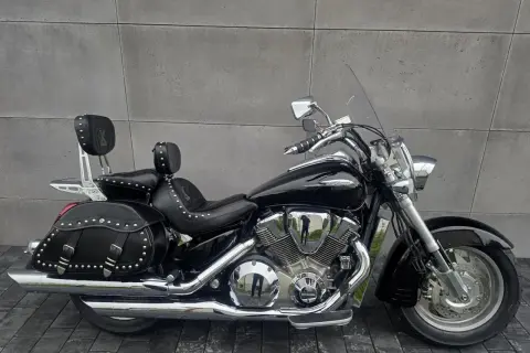 Czarny motocykl Honda VTX 1800 Neo z sakwami i oparciem dla pasażera, lśniący chromem na tle szarej ściany.