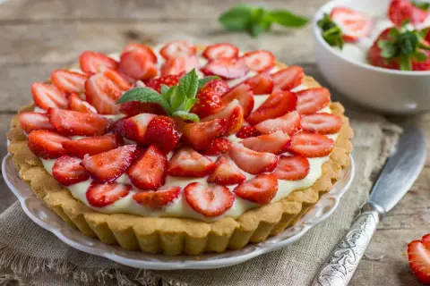 Prosta tarta z truskawkami, udekorowana listkami mięty, wygląda apetycznie na drewnianym blacie.
