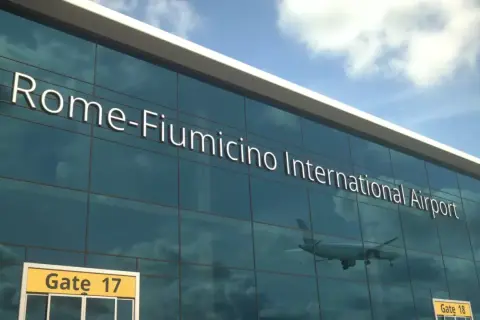 Szklana fasada lotniska Rome-Fiumicino International Airport, z odbijającym się samolotem i znakiem Gate 17.