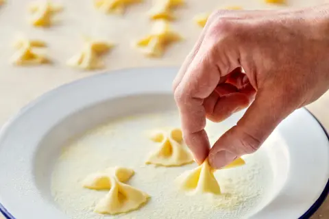 Hand formt frische Farfalle für leckere Farfalle Rezepte. Viele kleine Nudelschmetterlinge liegen bereit.