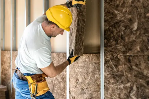 Operaio con casco giallo installa pannelli per l'isolamento acustico in una parete in costruzione.