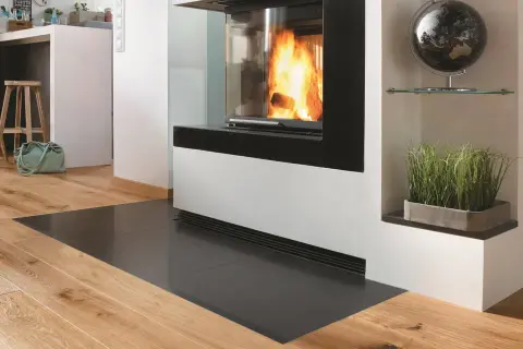 Moderner Kamin mit Sicht auf Flammen, geschützt durch eine Glasplatte. Die Bodenplatte des Ofens entspricht der Vorschrift für Brandschutz.