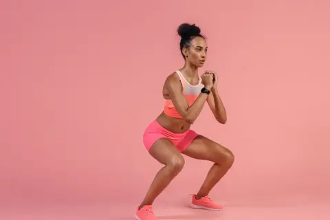 A woman in athletic wear performs pulsing squats, her hands clasped in front of her chest.