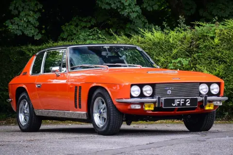 En orange Jensen Interceptor från 70-talet, en klassisk bil med en tidlös design, parkerad utomhus.