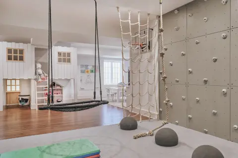 A child's indoor adventure zone with a climbing wall, net, and swing, embodying a Montessori aesthetic.