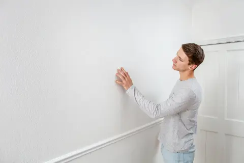 Man känner på en vit vägg, kanske för att ta bort tapet och måla om.