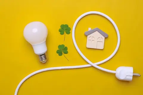 Bombilla, tréboles y un enchufe con forma de casa simbolizan el confort visual y la energía en el hogar.