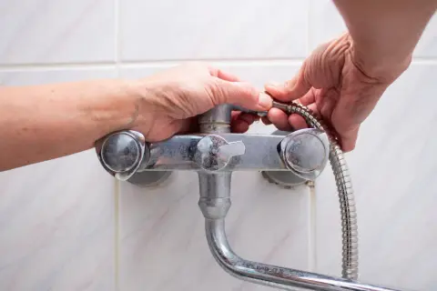 Hands working to fix a shower faucet, detaching the shower hose.