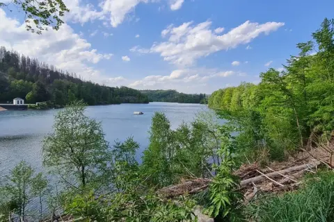 Ein ruhiger See mit einem kleinen Haus am Ufer, umgeben von grünen Wäldern. Der genkeltalsperre rundweg lädt zum Spaziergang ein.