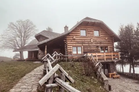 Drewniany dom z kamienną podstawą, kamienista ścieżka i płot. Mglisty dzień dodaje uroku temu miejscu, które oferuje liczne laskowa atrakcje.