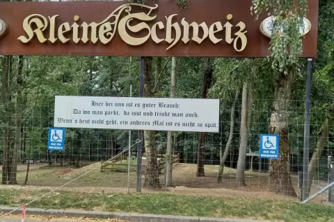 Schild "Kleine Schweiz" in Velbert. Ein Spruch lädt zum Verweilen ein. Parken, essen, trinken – perfekt für eine Wanderung.