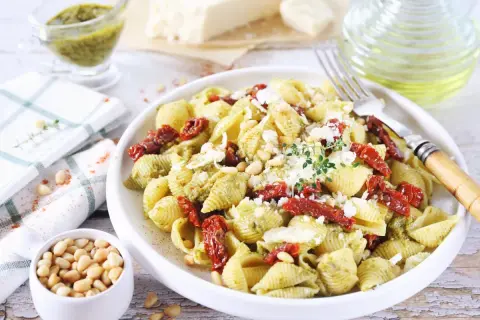 Pyszny makaron z pesto i suszonymi pomidorami, posypany parmezanem i orzeszkami pinii. Idealny na szybki obiad.