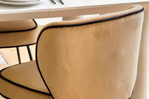 Chaises au revêtement velours couleur camel, bordées d'un passepoil noir, autour d'une table blanche.