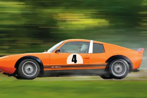 En orange Saab Sonett IV med nummer 4 på sidan susar fram på en bana, omgiven av suddiga gröna träd.