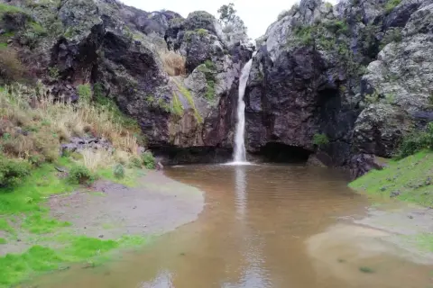 Cascada cayendo en el **charco de la paloma**, rodeado de rocas oscuras y vegetación.