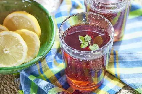 Un verre de jus de bissap pétillant, garni de menthe fraîche, à côté d'un bol de citrons tranchés. Parfait pour une journée ensoleillée.
