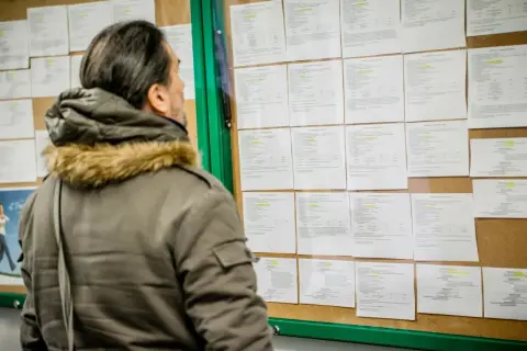 Mężczyzna w zimowej kurtce analizuje ogłoszenia na tablicy, szukając informacji o umowie zlecenie i składkach.