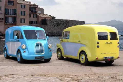 Två färgglada Morris bil-modeller, en blå och en gul, står vid havet.