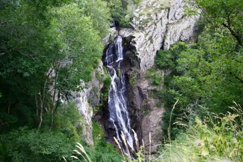 La cascade de Cubserviès dévale une falaise rocheuse, entourée d'une végétation luxuriante. L'eau blanche contraste avec le sombre des rochers.