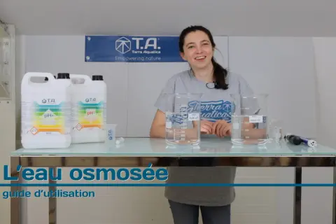 Une femme souriante présente des produits pour ajuster le pH de l'eau osmosée, avec des béchers et des bouteilles sur une table.