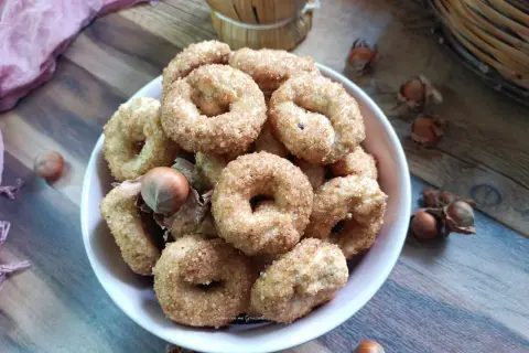 Ciambelline al vino ricetta originale, dorate e croccanti, con nocciole sullo sfondo.