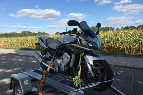 Srebrny motocykl Yamaha na przyczepce, na tle pola kukurydzy i błękitnego nieba z chmurami.
