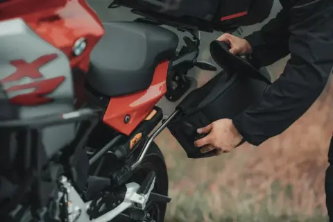 Mężczyzna montuje czarną sakwę motocyklową do czerwonego motocykla.