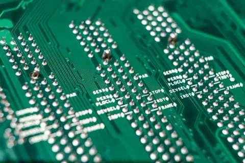 Zielona płyta drukowana z rzędami srebrnych pinów i oznaczeniami, świadectwo roli srebra w elektronice.