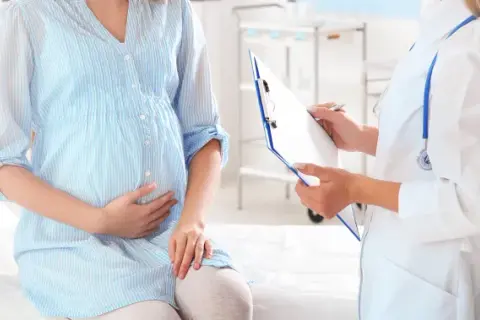 Lekarz spisuje dokumentację medyczną dla ciężarnej kobiety. Dowiedz się, co przysługuje kobiecie w ciąży bez pracy.