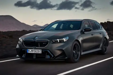Mroczny, matowy BMW M5 Touring pędzi po pustej drodze, z górami w tle.
