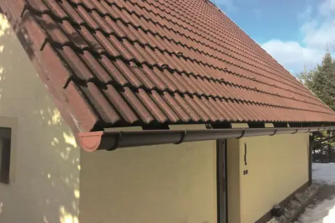 Brązowy rynna dachowa pod czerwonym, dachówkowym dachem domu.
