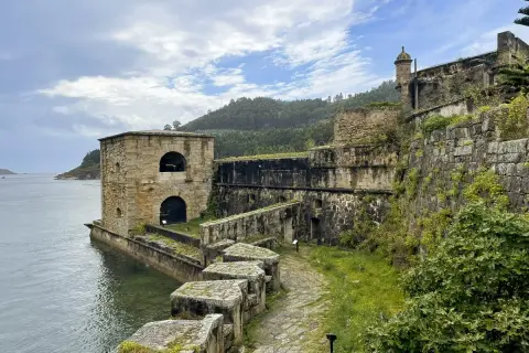 El castillo San Felipe en Ferrol, una fortaleza de piedra junto al mar, con vegetación cubriendo sus muros y un camino empedrado.