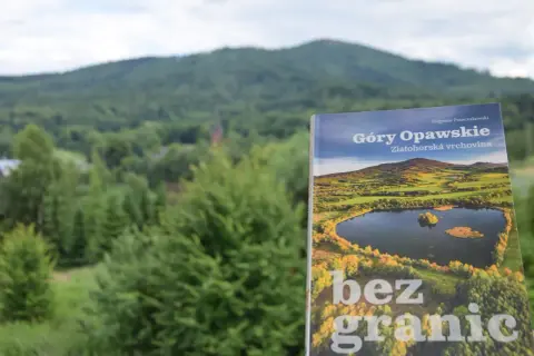 Książka "Góry Opawskie" na tle zielonych wzgórz. Okładka przedstawia malowniczy krajobraz z jeziorem i jesiennymi barwami.