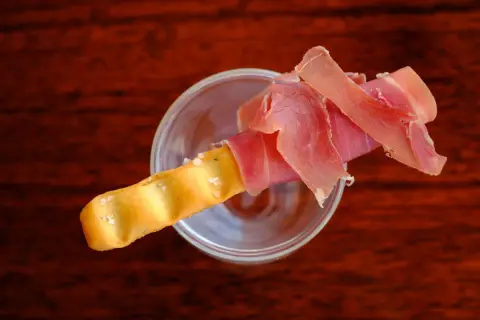 Ein knuspriger Grissini mit zartem Schinken, serviert in einem Glas.