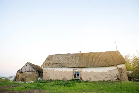 Dwa stare budynki gospodarcze na zgłoszenie, jeden z kamienia i drewna, drugi z tynkiem odpadającym od ścian, stoją na tle jasnego nieba.