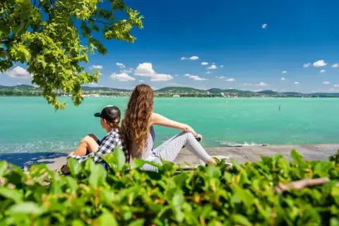 Dzieci siedzą plecami do widza, patrząc na turkusowe wody Balatonu na Węgrzech.
