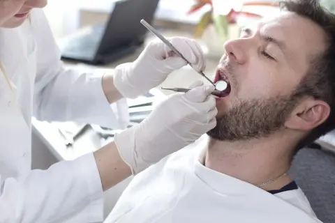 Dentysta bada zęby pacjenta. Rozważasz pokrycie recesji dziąsła NFZ? Wizyta u stomatologa to pierwszy krok.