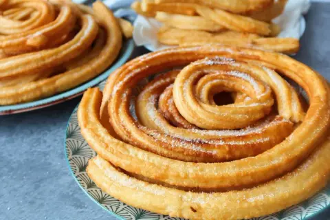 Churros dorados y azucarados en espiral en platos.