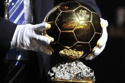 Złota Piłka FIFA Ballon d'Or na błyszczącym cokole, trzymana w białych rękawiczkach.