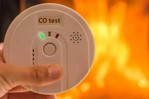 Détecteur de monoxyde de carbone tenu à la main, avec un feu de cheminée en arrière-plan. Où placer détecteur monoxyde de carbone ?