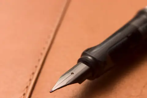 Plume d'un stylo plume noir sur un cuir brun. Une tache d'encre sur le cuir ? Apprenez comment enlever du stylo sur du cuir.