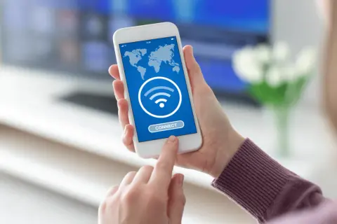 Dłoń trzyma smartfon z mapą świata i ikoną Wi-Fi. Dotyka przycisku "CONNECT", szukając darmowego hotspotu.