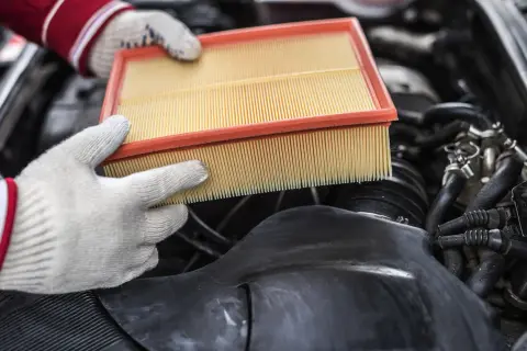Mains gantées tenant un filtre à air propre, prêt à remplacer un filtre à air encrassé dans un moteur de voiture.